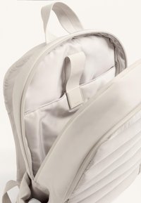 Világosszürke hátizsák sima, párnázott külső résszel és puha belső béléssel. Állítható vállpántokkal és egy kis téglalap alakú fémrészlettel rendelkezik.