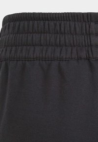 Pantalons noirs avec une taille élastique froncée et une texture lisse. Le tissu semble doux et durable, adapté à un usage décontracté.