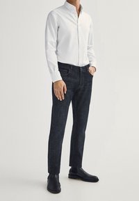 Camicia bianca con bottoni, jeans in denim scuro e stivali neri alla caviglia. Vestibilità dritta, tessuto morbido e design del colletto classico.