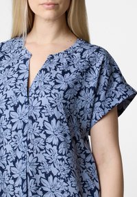 Lyhythihainen paita vaaleansinisellä kukkakuviolla, joka on tummansinisellä pohjalla. Malleissa on V-pänä ja rento istuvuus. Valmistettu pehmeästä, hengittävästä kankaasta.