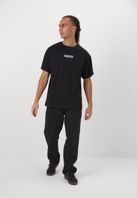 Black cotton t-shirt with short sleeves, featuring "JUVENTUS" logo in white. Paired with black loose-fit jeans and black sneakers.