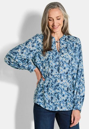 Blaue Musterbluse mit Schlitzkragen, langen Ballonärmel und einem leichten Stoff mit einer weichen, fließenden Textur.