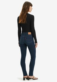 Vaqueros ajustados de color azul con una cintura alta, que presentan un clásico parche de cuero en la parte trasera, costuras detalladas y una textura de denim suave y duradera.