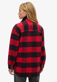 Camicia in flanella a quadri rossi e neri con maniche lunghe, colletto e polsini con bottoni in pressione, caratterizzata da un orlo a maglia e uno yoke posteriore.