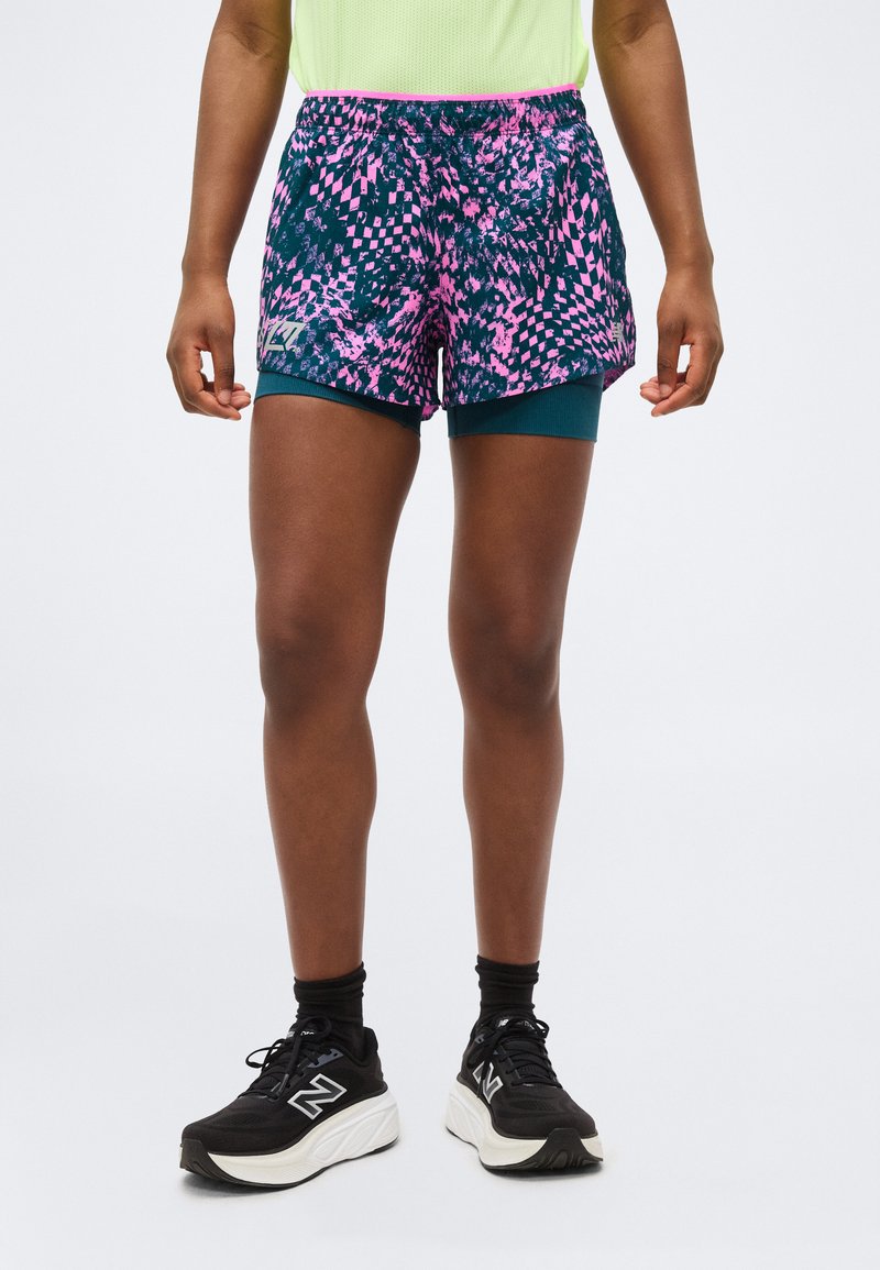 Personne portant un short de sport à motifs roses et marine avec un short de compression turquoise en dessous, des chaussettes noires et des chaussures de course noires.