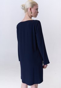 Navyblaues, langärmeliges Kleid mit gerader Passform und Bootsausschnitt. Glatte Textur, knielang, mit einem leichten Saum.