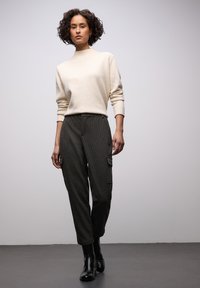 Roomkleurige coltrui gecombineerd met donkere geruite cargobroek met zijzakken en zwarte enkellaarsjes, met een moderne, ontspannen pasvorm.