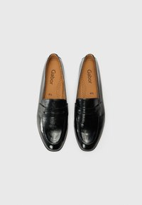 Mocassins en cuir noir avec une texture lisse, dotés de détails cousus et d'un design à enfiler. L'intérieur comprend une semelle intérieure matelassée avec le nom de la marque.