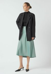 Mustmust kattega mustkübersärk pealt tiheda musta toppi, mis on ühendatud voolava münti rohelise seeliku ja mustade terava nina kontsadega. Sujuvad tekstuurid ja moodne disain.