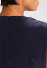 Robe marine en tissu satin lisse, col rond, et fermeture éclair discrète à l'arrière. Design minimaliste avec des lignes épurées.