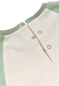 Top de mezcla de algodón con un cuerpo en crema y mangas raglán verdes. Cierre a presión en el escote con una sutil textura y detalles.