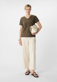 Olivengroen katoenen T-shirt met V-hals, gecombineerd met crèmekleurige wijde broek. Geaccessorieerd met een kleine witte tas en zwarte sandalen.