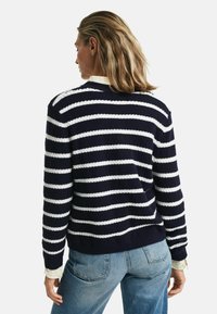 Marinblå och vit randig tröja med ett texturerat stickmönster, rundad halsringning och ribbade ärmslut, kombinerad med ljusblå denimjeans.