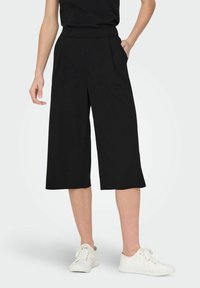 Svarta culotter med breda ben, hög midja och framvikt, gjorda av ett slätt tyg, i kombination med vita sneakers.