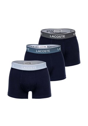 Trois paires de boxers Lacoste bleu marine avec des ceintures élastiques en gris, bleu et bleu clair, chacune arborant le logo Lacoste.