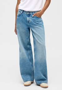 Gaišzilās plaša kāju džinsi izgatavoti no denima, ar augstu jostasvietu, priekšējām kabatām un izbalējusi mazgāšanu. Apakšmalas ir nedaudz safrētas.