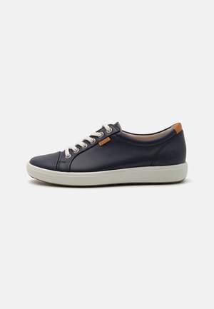 Sneaker in pelle blu navy con lacci beige, suola in gomma bianca e un accento in pelle marrone chiaro sul tallone. Punta arrotondata e design minimalista.