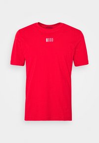 Lys rød kortærmet T-shirt med lille hvid "HUGO" logo centreret på brystet mod en ensfarvet hvid baggrund.
