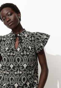 Blouse à motifs noir et blanc avec des manches volantées, un col en forme de trou de serrure et des motifs floraux. Fabriquée en tissu léger avec une finition texturée.