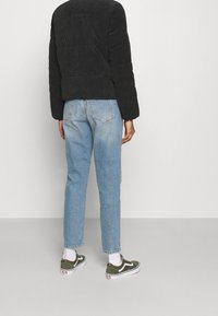 Svart kordjacka, ljusblå raka jeans och gröna Vans-sneakers med vita detaljer, sedd bakifrån.