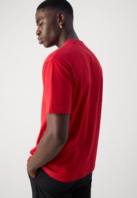 Red cotton t-shirt with short sleeves, round neckline, and a relaxed fit. Seam details on shoulders and a smooth texture.