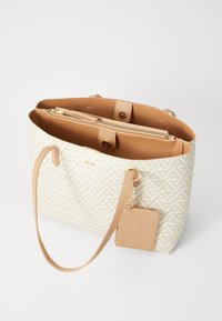 Sac fourre-tout beige à motifs avec des accents en cuir marron clair, équipé d'une poche zippée à l'intérieur et d'une étiquette amovible attachée par une lanière.