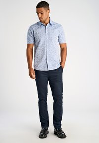 Camicetta azzurra a maniche corte con un motivo circolare, abbinata a pantaloni blu scuro e scarpe nere. Design semplice e colletto abbottonato.