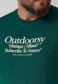 Baardman in een groene shirt met crème tekst: "Buitengevoelens Vooruit! Abonneer je op de Natuur. Word lid van S.Oliver & Friends."