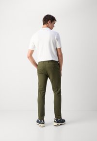 Herreoutfit med en hvid polo shirt og olivengrønne slim-fit bukser. Bemærkelsesværdige detaljer inkluderer baglomme og kontrasterende sneakers.