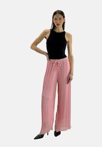 Hellrosa plissierte Hose mit elastischem Bund und Kordelzugdetail, kombiniert mit einem schwarzen ärmellosen Oberteil und schwarzen spitzen Absatzschuhen.