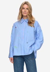 Camicia azzurro chiaro in cotone con ricami di diversi colori tra cui cuori e testo, maniche lunghe e taglio morbido.