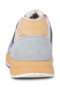 Vue arrière d'une basket en cuir beige avec des panneaux en daim bleu clair, semelle beige et logo WODEN embossé sur le talon.