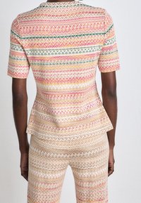 Ensemble top peplum multicolore et pantalon avec un motif en zigzag rose, crème, orange et vert. Manches courtes et tissu texturé.