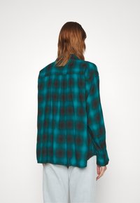 Camicia di flanella turchese con motivo a quadretti neri, maniche lunghe e vestibilità rilassata. Caratterizzata da uno yoke posteriore e polsini con bottoni.