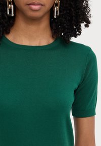 Grøn kortærmet striktop med rund halsudskæring. Stoffet er glat med en blød tekstur og har diskrete ribbede kanter.
