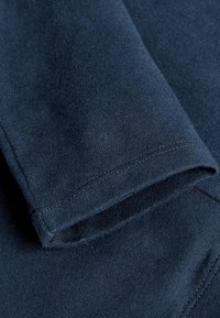 Tissu en coton bleu marine foncé avec une texture lisse, présentant une manche pliée et des détails de couture en ourlet. Pas de motifs ni d'accents supplémentaires visibles.