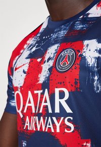 Sportovní dres v červené, modré a bílé barvě s abstraktními vzory, logem Nike a nápisem "Qatar Airways". Odznak zní "PARIS SAINT-GERMAIN."