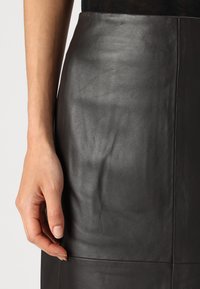 Svart skinnskjørt med en glatt tekstur, høy midje og tettsittende design. Har pent søm og en ren, moderne silhuett.