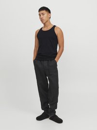 Débardeur noir, pantalon sombre ample et chaussures foncées. Le débardeur présente un col rond et un design sans manches, avec une texture de tissu douce.