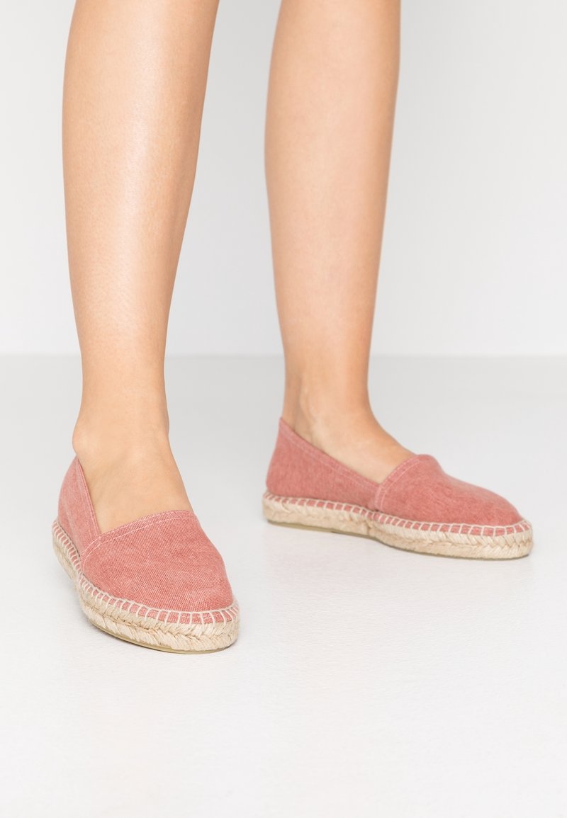 Espadrilles en toile rose avec semelles en jute, présentant une texture lisse, un design à enfiler et des coutures exposées le long du bord.