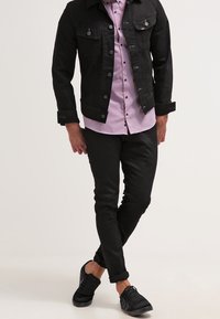 Musta farkkutakki napillisen edustan kanssa, vaaleanpunaraidallinen paita, mustat slim-fit-housut ja mustat lenkkarit. Minimalistinen muotoilu ja istuva malli.