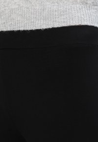 Juodi leggingai su lygiu paviršiumi, derinami su šviesiai pilku, raukšlėtu megztiniu, turinčiu trumpą apačią ir laisvą siluetą.