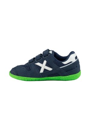 Zapatilla deportiva azul marino con suela verde, logo "X" blanco en el lateral, tres tiras de velcro y detalles blancos en la zona del talón.