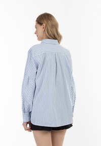 Lyseblå og hvidstribet skjorte med krave, puffede ærmer og en plisseret rygdesign, parret med sorte slidte shorts.