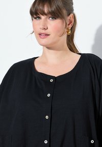 Camicia nera, dallo stile morbido, con scollatura rotonda e bottoni sul davanti. Tessuto leggero con una texture sottile, dotato di due tasche laterali.
