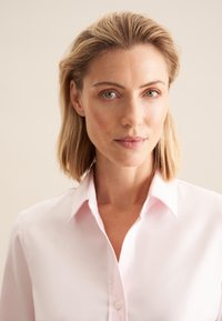 Camicia button-up rosa chiaro con colletto classico, realizzata in tessuto morbido. Presenta una trama delicata e un design aderente.