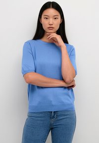 Lichtblauwe gebreide trui met korte mouwen, ronde halslijn en geribbelde details, gecombineerd met lichtblauwe spijkerbroek.