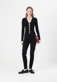 Svart langermet bodysuit med dyp V-hals og frontlukking, kombinert med tettsittende svarte jeans og glansete svarte loafers. Rød veske som aksent.