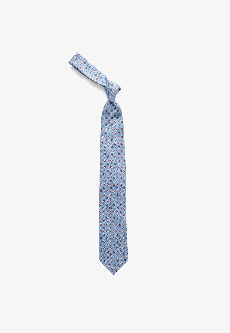 Cravate bleu clair avec motif floral circulaire rouge et blanc, nouée de manière lâche, affichée sur un fond blanc.