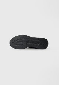 Semelle de sneaker noire avec surface en caoutchouc texturé, présentant un motif de crantage distinct pour l'adhérence et la durabilité, bords lisses et sans marquages visibles.
